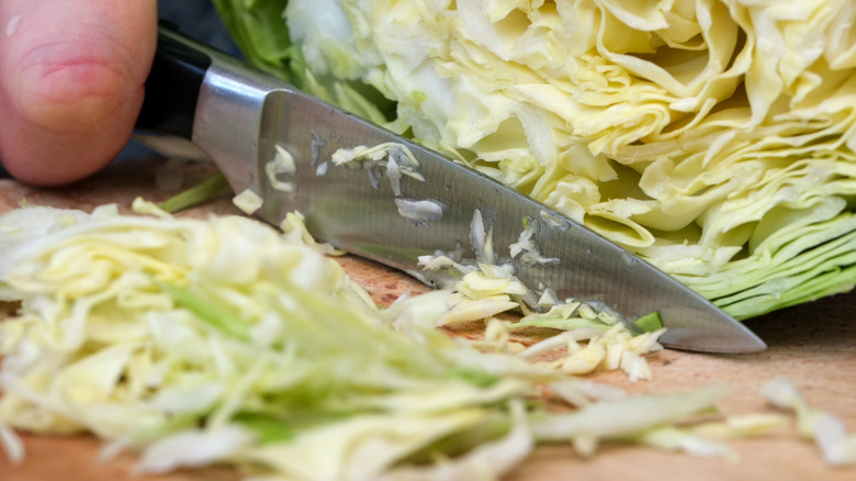 A hand cutting cabbage with a knife on a wooden board