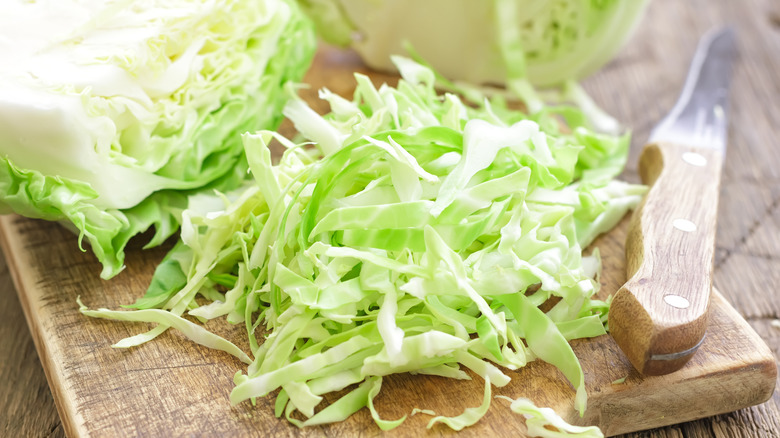 Shredded cabbage and a knife on a wooden cutting board