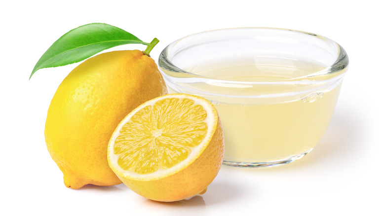 Lemon juice in bowl next to sliced lemon on white background