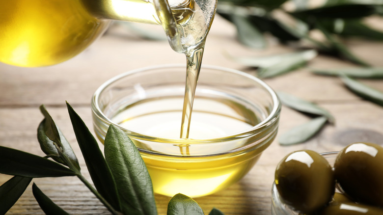 Olive oil pouring from glass jug into bowl