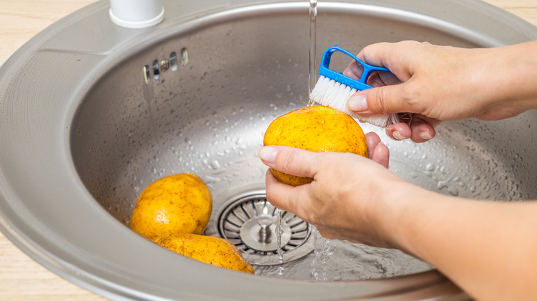 Hands scrubbing potatoes under stream of water from sink