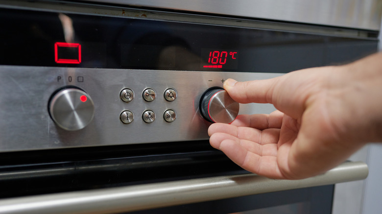Hand turning dial on oven to preheat it