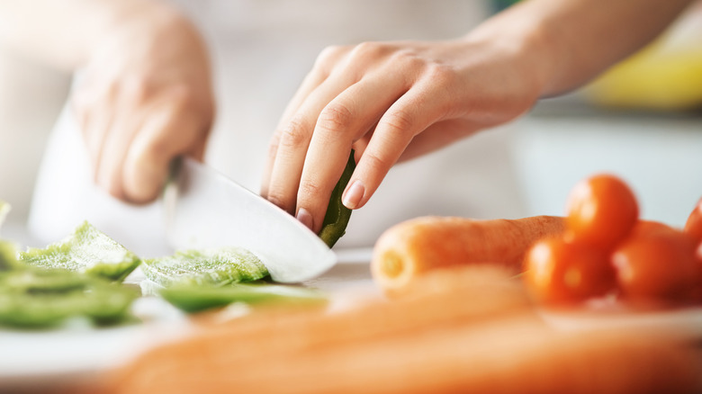 Hands chopping vegetables on wooden cutting board