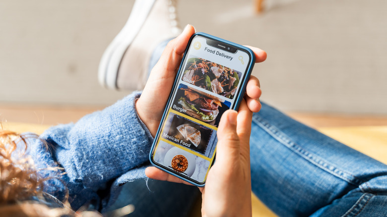 Person's hands holding phone with food delivery app on screen