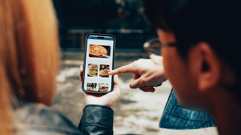 Person pointing at food delivery app on phone with friend