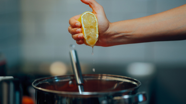 A hand squeezing a lemon into a pot of soup