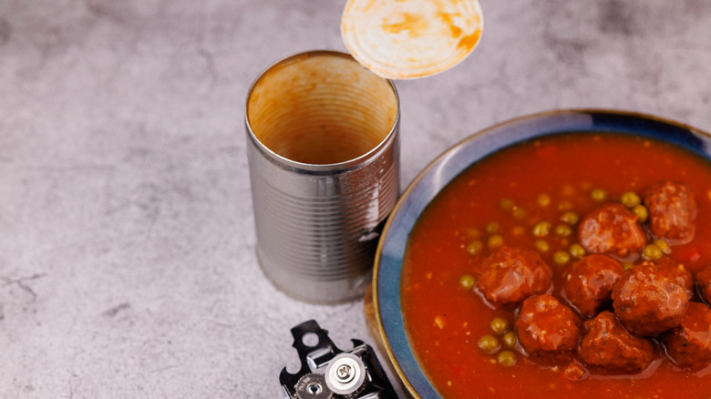Open can of soup next to bowl with meatballs and peas