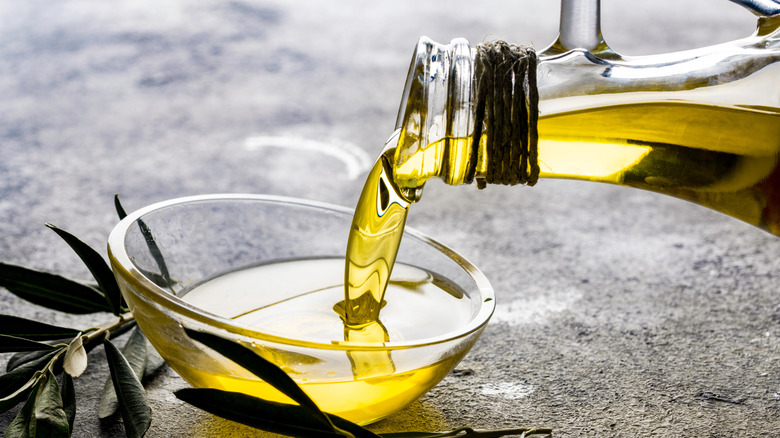 A bottle of olive oil pouring out into a glass bowl