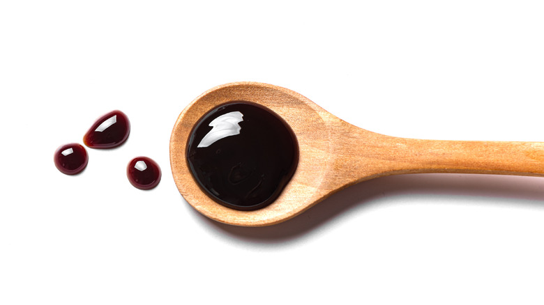 Soy sauce on wooden spoon on white background