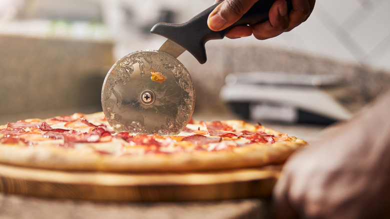 Cutting pizza with pizza wheel on a wooden cutting board