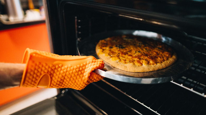 Oven gloved-hand taking pizza out of oven