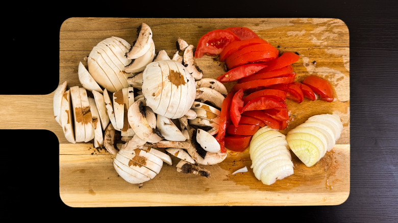 Sliced mushrooms, pepper, and onions on wooden cutting board