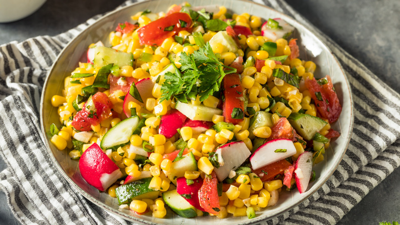 Bowl of corn salad with radish, cucumber, tomato, and parsley
