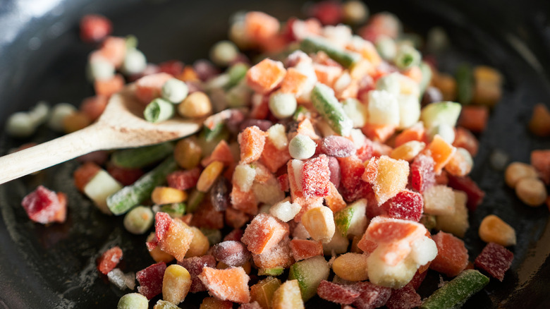 Frozen vegetables in frying pan with wooden spoon