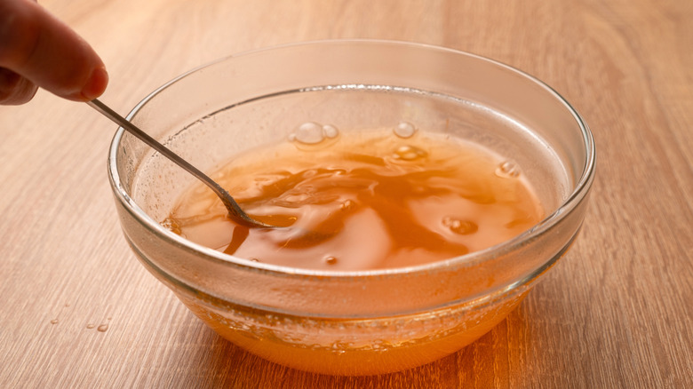 A bowl of gelatin solution getting mixed with a spoon