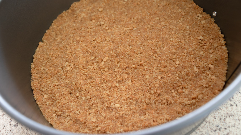 A cake pan filled with graham cracker crust