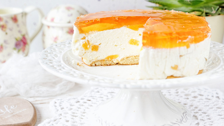A whole peach cheesecake on a cake stand with a slice cut out
