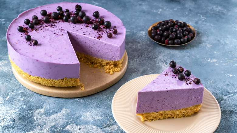 Whole blueberry cheesecake with a slice cut out of it