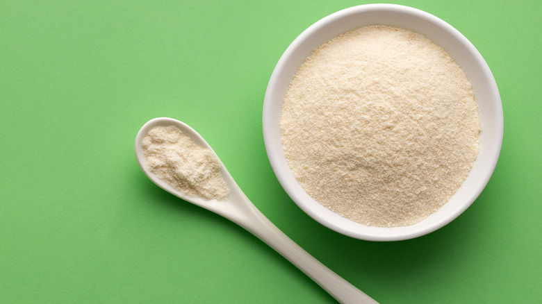 A bowl and spoon filled with gelatin powder on a green background