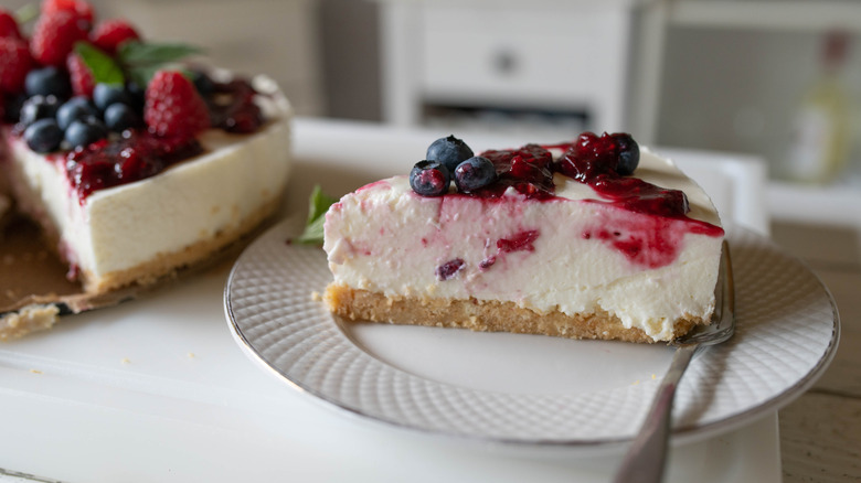 A slice of no bake cheesecake topped with berries with the whole cake in the back