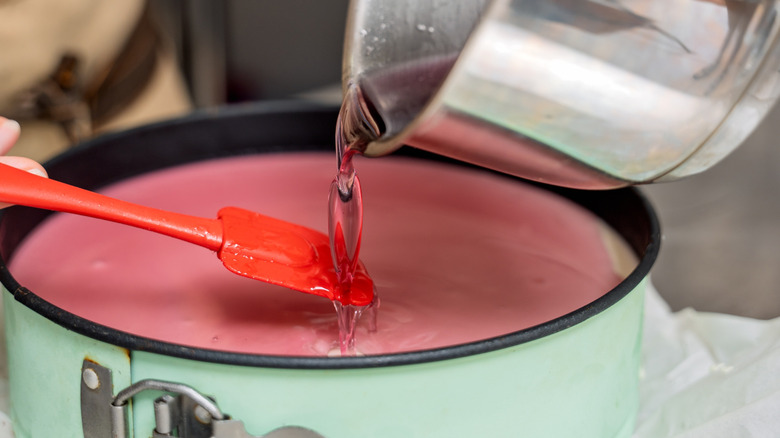 Someone pouring sauce into a springform pan filled with cheesecake