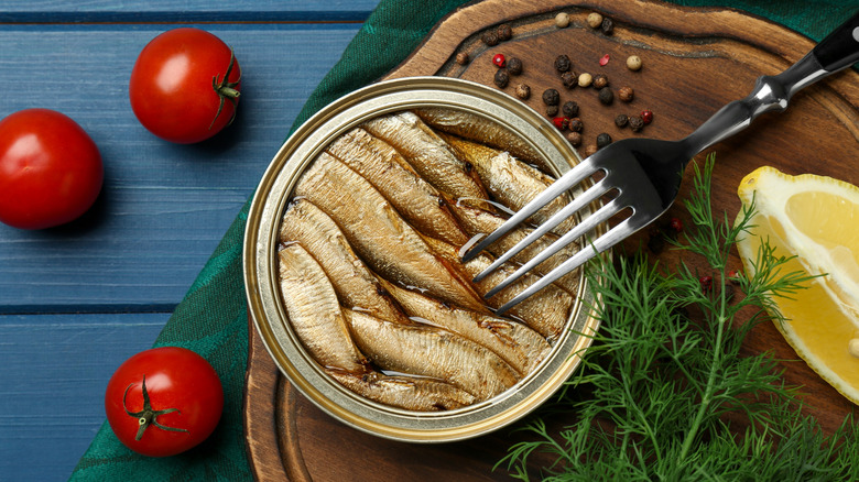 Opened can of fish next to tomatoes, lemon slice, and fresh dill