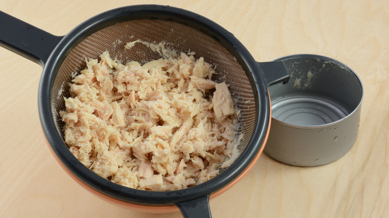 Canned tuna in strainer next to empty metal tin