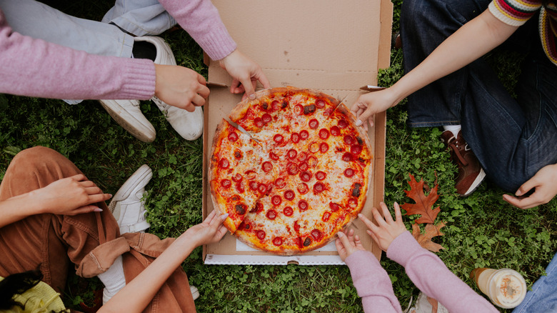 Hands reaching for a takeout pizza on the grass