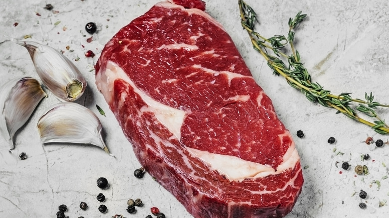 Raw ribeye steak with rosemary, peppercorns and garlic cloves on the side