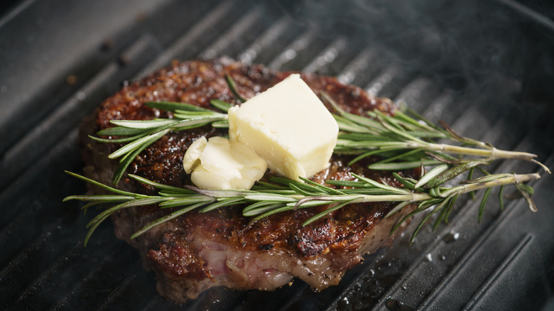 Ribeye steak on a grill pan with butter and rosemary