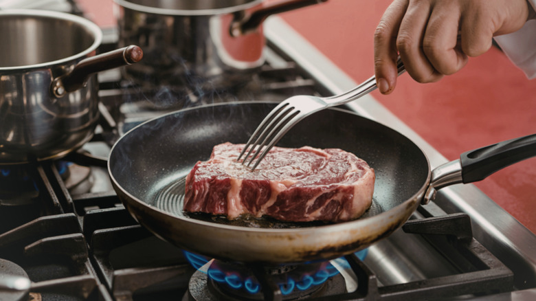 person searing a raw steak in a nonstick pan