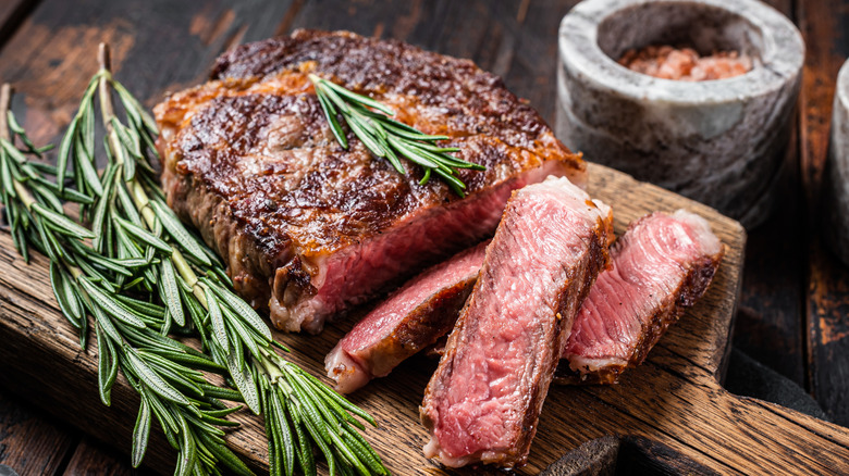 Grilled and sliced ribeye steak on a wooden board with rosemary sprigs