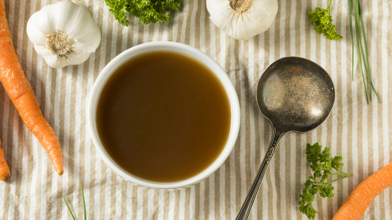Beef broth in white bowl surrounded by ingredients and spoon
