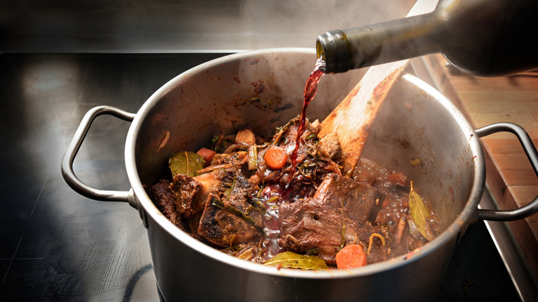 Red wine pouring into pot of beef and vegetables to deglaze it