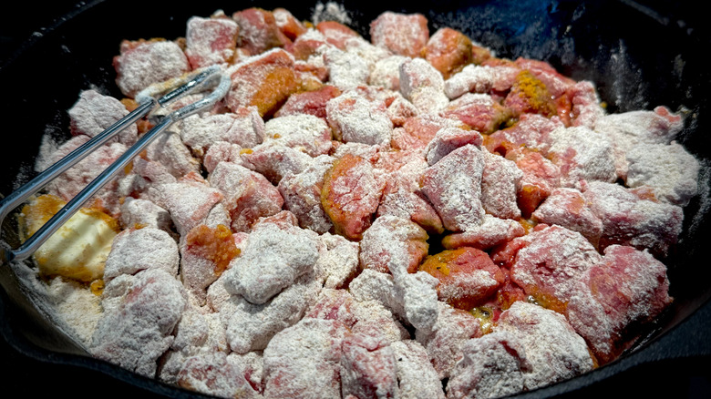 Flour-coated pieces of beef browning in pan