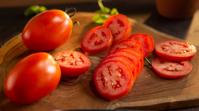 Sliced and whole tomatoes on wooden cutting board