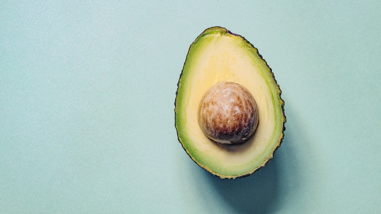 Half an avocado with pit on blue background
