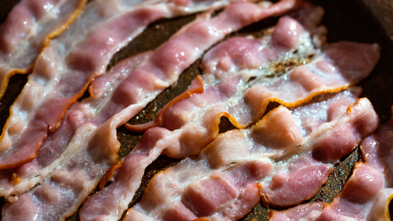 Soggy bacon cooking in black pan