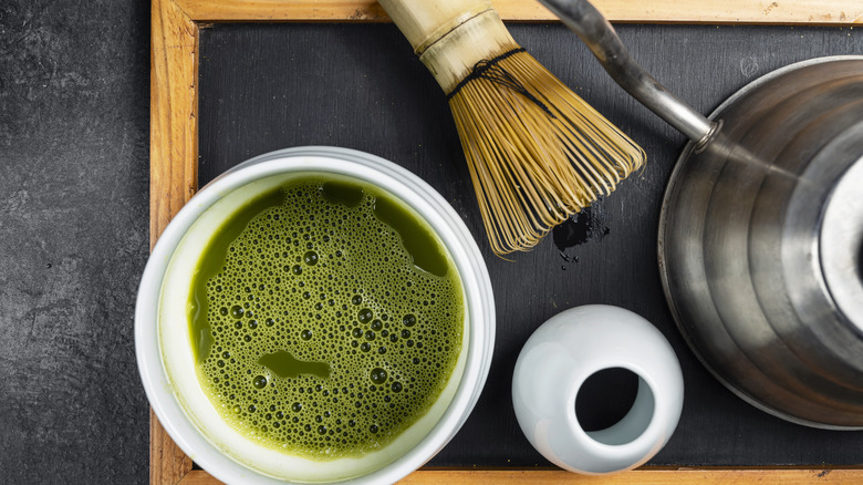 A cup of matcha next to a whisk and tea pot