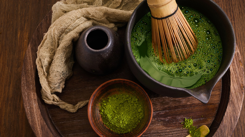 A tray of matcha powder and a bowl of matcha with a bamboo chasen