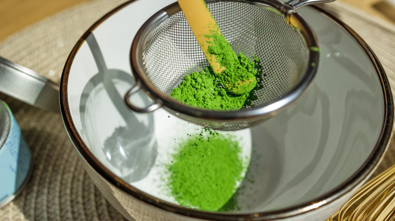 Matcha powder being sifted through a sieve into a cup