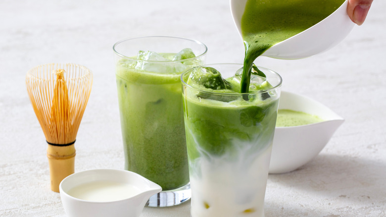 Two matcha lattes in tall glasses with one having the matcha poured in