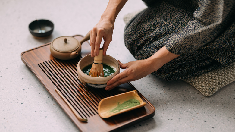 Someone kneeling down and whisking matcha with a bamboo whisk