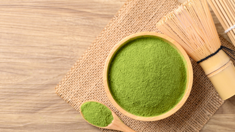 Matcha powder in a wooden bowl and spoon with a bamboo whisk