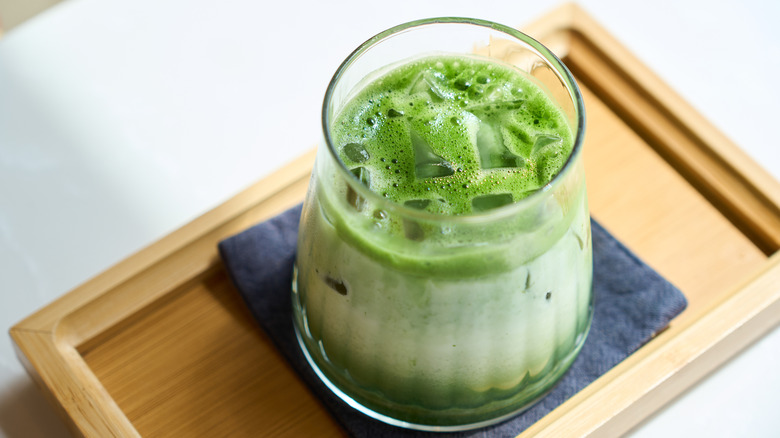An iced matcha in a glass on a wooden tray