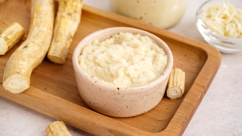 Horseradish in white bowl on wooden cutting board