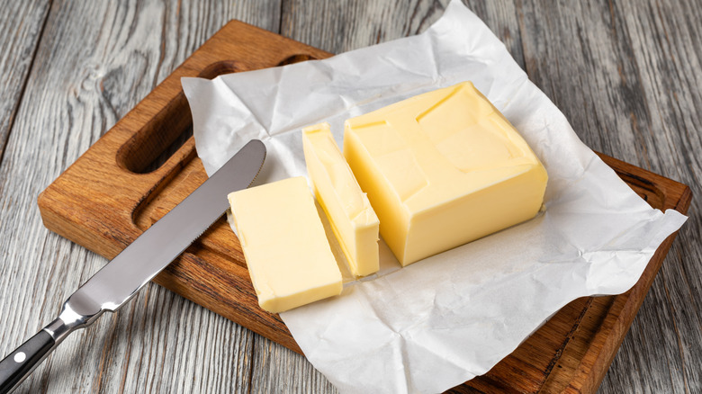 Cut stick of butter on wooden cutting board with knife