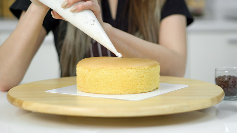 Person piping white frosting onto vanilla cake