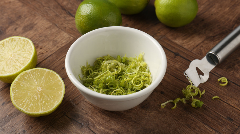 Lime zest in small white bowl with limes