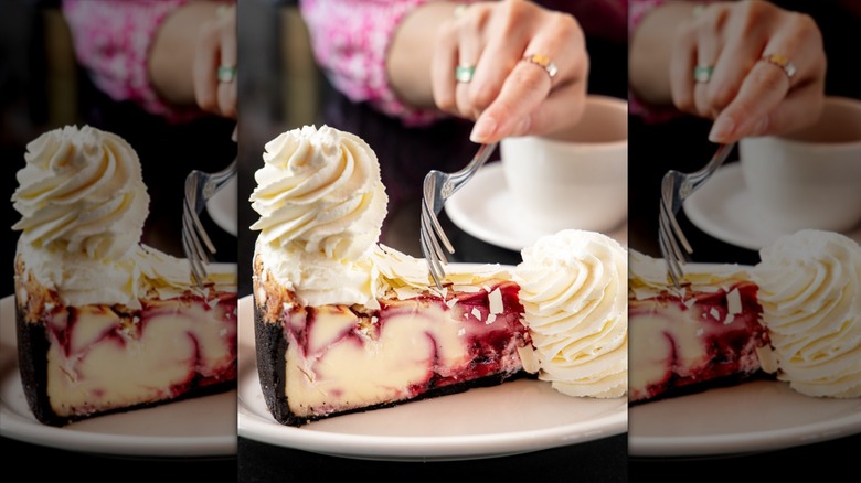 Fork cutting into raspberry cheesecake on white plate